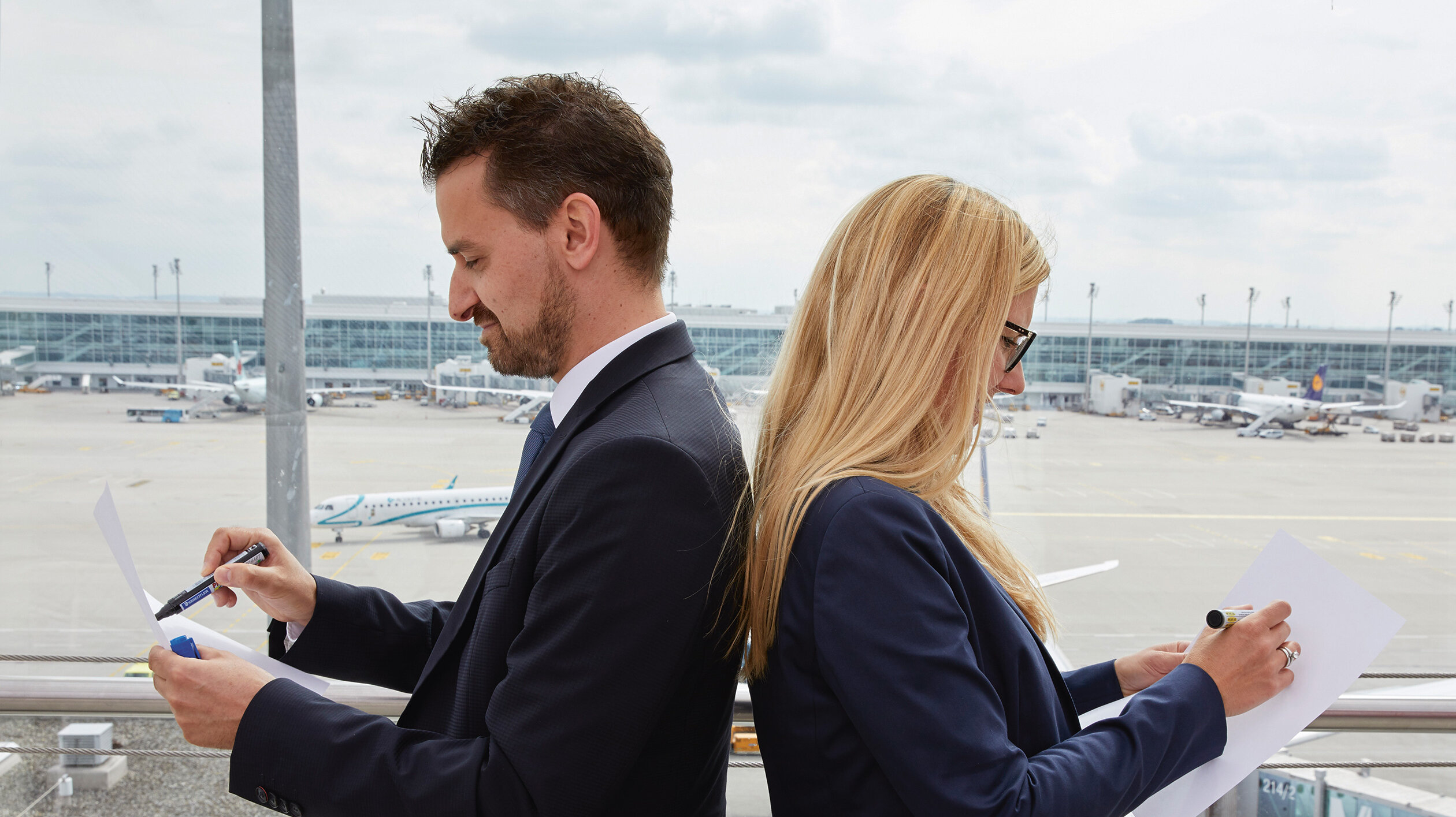 Ein Paar Rücken an Rücken vor einem Fenster mit Blick auf das Vorfeld Ein Paar Rücken an Rücken vor einem Fenster mit Blick auf das Vorfeld